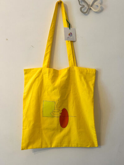 Υφασμάτινη tote bag σε φωτεινό κίτρινο χρώμα με σχέδιο καφέ φλιτζάνι προσθέτει μια παιχνιδιάρικη και ζωντανή πινελιά στις εμφανίσεις σας. Ευρύχωρη και ανθεκτική, είναι ιδανική για την βόλτα, τα ψώνια και την σχολή.